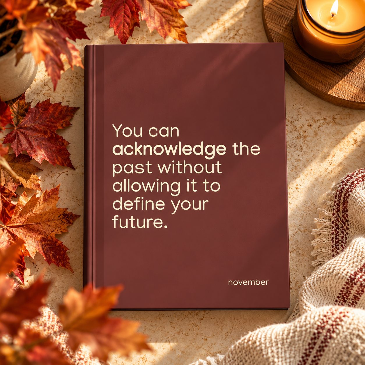 Burgundy November hardcover journal with cream inspirational quote, surrounded by autumn leaves, a knit blanket and candle