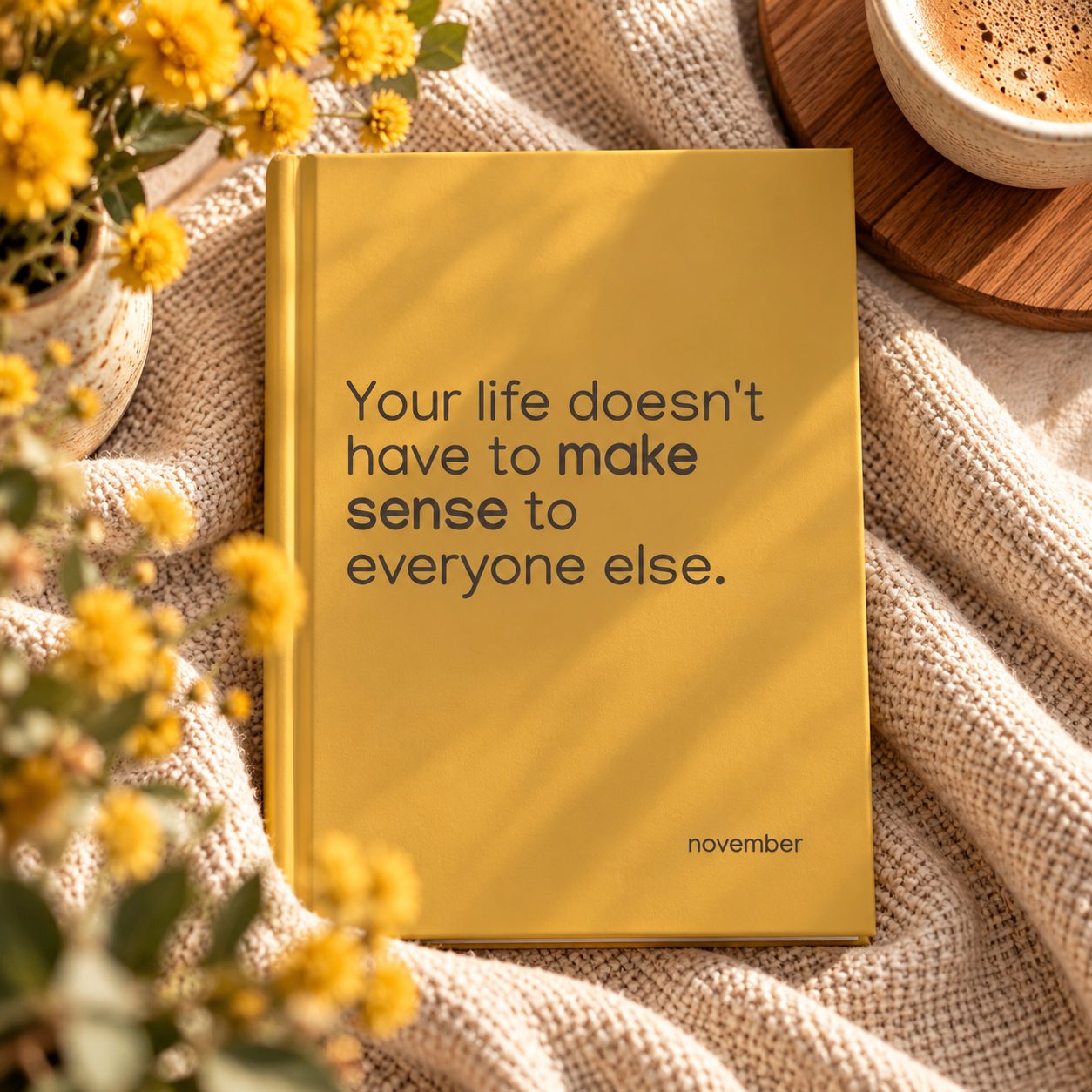 Golden November hardcover journal on a knitted blanket beside coffee and yellow flowers with an inspiring cover quote