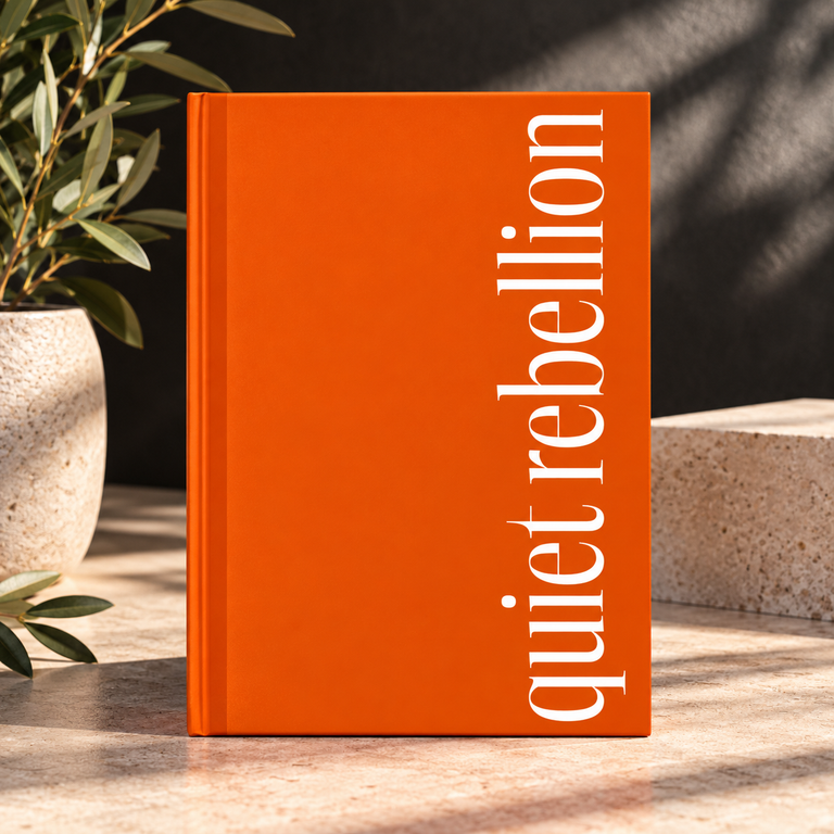Orange hardcover journal titled "Quiet Rebellion" standing on a stone tabletop with plant and textured backdrop