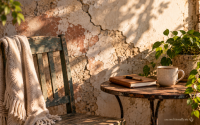 Sunlit patio scene showing cracked plaster wall, distressed wooden chair with blanket, journal and coffee cup